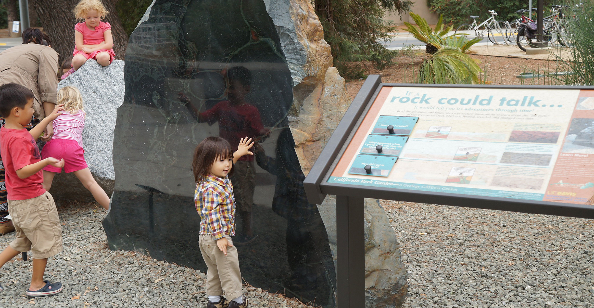 Child admiring a large rock outdoors.