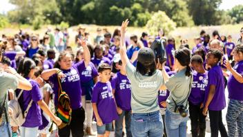 Two student interns get the attention of a large group of students in the Arboretum.