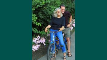 Kent Bradford and Barbara Zadra posing together on a bike in their garden.