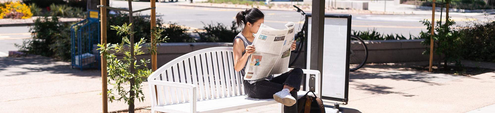 person reading the newspaper on a bench